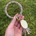 Détail du porte-clés bracelet en cuir à carreaux avec fermoir doré et glands sur l'herbe - Grille Colorée