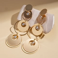Détail de boucles d'oreilles dorées géométriques avec zircons sur une pierre grise - Doré