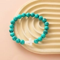 Turquoise beaded bracelet featuring a white cross pendant on a textured beige tray - Blue Turquoise White Cross Bracelet