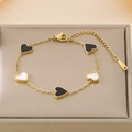 Detalle de pulsera dorada con corazones de nácar blanco y negro en estuche de joyería - Negro y Blanco (KB187177-BI)