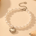 Detalle de colgante de corazón plateado y perlas blancas en pulsera de acero inoxidable - Color Acero