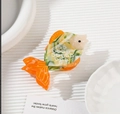 Gros plan d'une pince à cheveux poisson en acétate avec nageoires orange et effet marbré - Vert