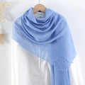 Detail of blue crinkled cotton linen scarf with raw fringe edges hanging on a hanger - Blue