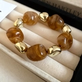 Retro elastic bracelet with amber resin beads and gold metal spheres on a beige base - Brown