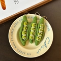 Three handmade green wool felt pea pod keychains with smiling faces on a cream plate - Pea Pod Trio