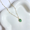 Detail van een 14K vergulde ketting met groene ovale steen op een golvend dienblad - Afrikaanse Jade