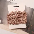 Detailed view of three champagne satin scrunchies displayed on a white branded card - Champagne