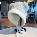 Dettaglio di un cappello di peluche bianco con orecchie da orso e lacci sul supporto - Bianco Sporco