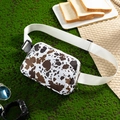 Detail shot of a lightweight cow print waist bag placed on a green picnic setting. - Cow White