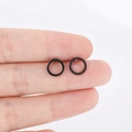 Close-up of minimalist black stainless steel hoop earrings held by hand for scale - Black
