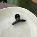 Detail view of the black glossy hair clip on a beige plate with leaf background - 5.5cm Butterfly Buckle / Glossy Black
