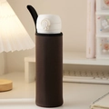 Brown insulated cup sleeve with black handle strap shown on a cozy desk setting - Coffee