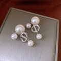 Close-up of pearl earrings with crystal-inlaid CD logo on a grey jewelry box surface - Silver Double Pearl CD Style
