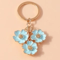 Detailed shot of golden keychain with three light blue enamel peach blossom charms - Blue