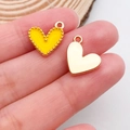 Macro view of tiny yellow enamel and gold heart charms held on fingertips for DIY jewelry - Peach Heart