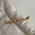 Dettaglio di un fermaglio dorato ondulato con perla bianca su lino beige naturale - Stile Corto-Oro / Perla grande singola