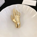 Makroaufnahme einer goldenen Hand-Brosche mit Hochglanz-Finish auf einem Keramikteller - Gold