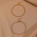 Close-up of gold layered ankle bracelets with crystal inlay on a champagne silk fabric - Figaro Chain And Rhinestone Thin Chain / KC Gold