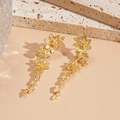 Detail van gouden bloemenoorbellen met glanzende strassteentjes op een lichte steen - Zilveren Pin-Gouden Bloem Oorbellen
