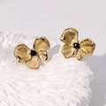 Close-up of golden bow earrings with black center detail on textured white surface - Black