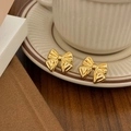 Detailed view of vintage gold bow earrings with radial texture on a ceramic cup edge - Gold Bowknot Stud Earrings