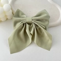 Close-up of sage green satin bow hair clip with smooth silk texture on ceramic tray - Green