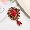 Detailed close-up of a vintage crystal brooch with a red teardrop gemstone and gold setting - Red