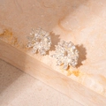 Macro-opname van zilveren bloem oorknopjes met zirkonia en parels op beige natuursteen - Zilveren Pin - Zilveren Bloem Zirkoon Oorknopjes