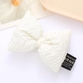 Close-up of a white padded puff pleated bow accessory with black woven label detail - White