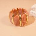 Detailopname van onregelmatige roze harssegmenten en gouden metalen staven op de armband - Paars