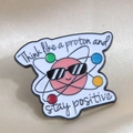 Pin de esmalte de protón rosa con la frase Think like a proton and stay positive - Think like a proton and stay positive (Letra 2)