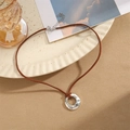 Nahaufnahme eines silbernen Hammerschlag-Anhängers an einer braunen Wildlederimitat-Kette - Silber Gehämmert Ring/Braune Kordel