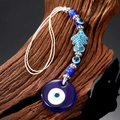Ethnic Evil Eye charm with blue glass and fish detail on rustic wood background - Small Fish Eye