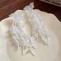Detalle de pendientes de flor blanca con borlas largas de cuentas en un plato de cerámica - Blanco