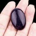 Polished oval blue goldstone cabochon held in hand showing size and sparkle - Blue Sand Stone (Synthetic)