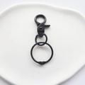 Detail view of a matte black metal lobster clasp and swivel rings on white ceramic - Black