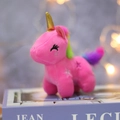 Plush pink unicorn keychain with golden horn and rainbow mane on decorative book - Red