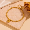 Dettaglio del bracciale a catena con sfere dorate e ciondolo su sfondo seta - Bracciale dorato (C104)