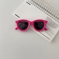 Close-up of pink children's sunglasses with black lenses on a white notebook background - Rose Red
