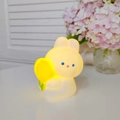 Cute cartoon rabbit night light in soft silicone with warm yellow glow on white desk - Tulip Rabbit