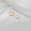 Close-up of gold geometric hoop earrings with white enamel on soft white silk fabric - White