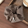 Close-up of brown striped fabric scrunchie with woven label on a wooden tray - Striped/Herringbone Texture / Coffee