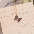 Vue détaillée du pendentif papillon violet avec chaîne dorée sur fond de pierre - Violet foncé