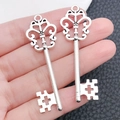 Detail of two vintage silver alloy key pendants with bow hollow-out design held in hand - Fan Shaped Key (9056)