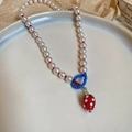 Detalle de collar de cuentas coloridas con colgante de fresa roja en un plato de cerámica - Collar con colgante de fresa esmaltado de cuentas de vidrio y perlas