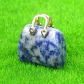 Miniature blue and white mottled stone handbag charm with a golden handle on green grass - Sodalite