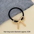 Elastic black hair tie with a textured metallic gold bow charm, 5cm outer diameter - Twisted Bow