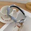 Light blue pleated twisted headband with faux pearls and rhinestones on a white cup - Blue