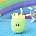 Macro view of green furry monster plush pendant with cute embroidered face and yellow crown - Milk Tea