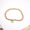 Detail eines Goldperlen-Armbands mit mintgrünem Herzanhänger auf weißem Satinband - Grün
